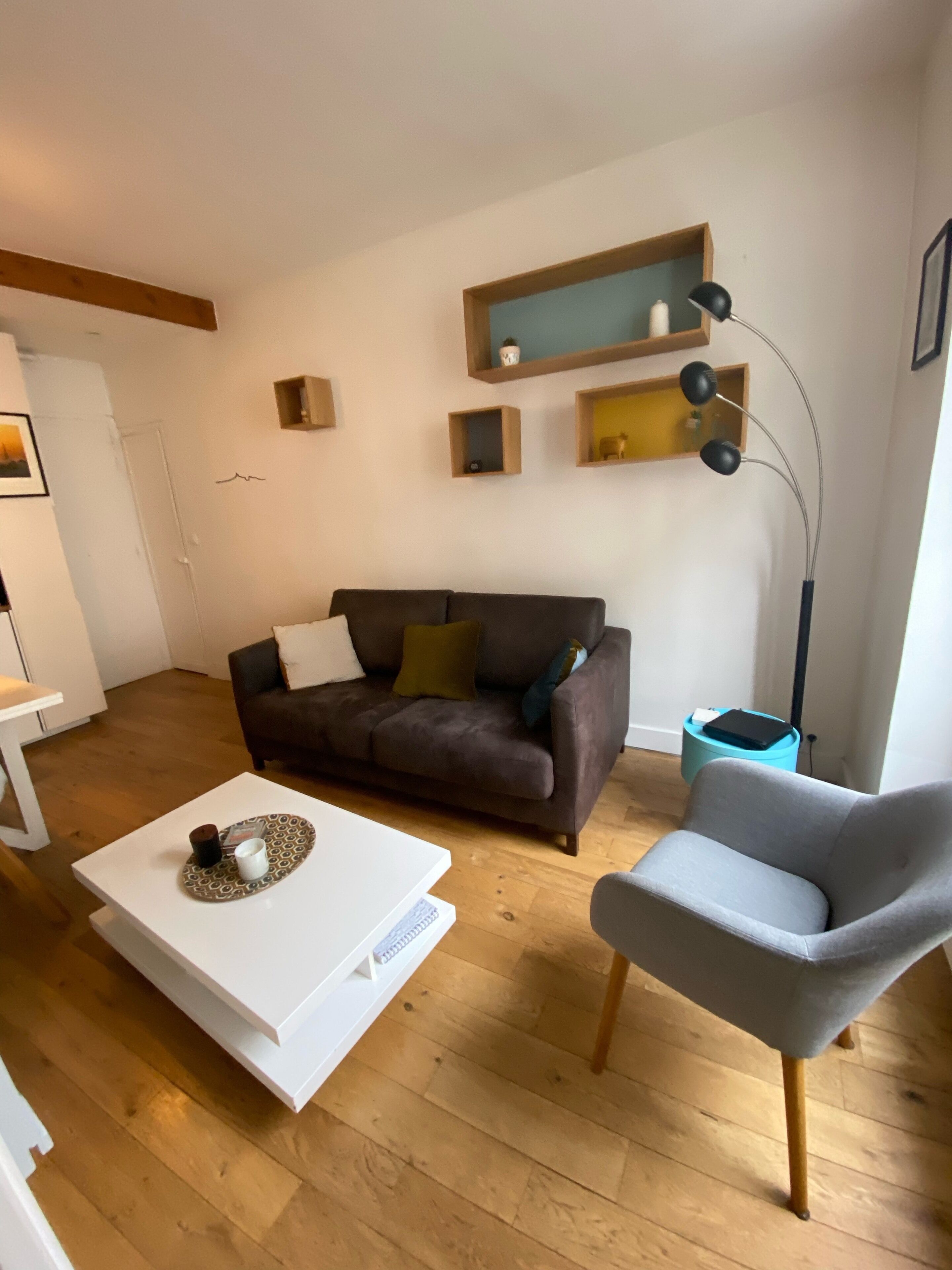 Un salon avec un canapé marron, un fauteuil gris, une table basse blanche et un lampadaire.
