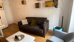 A living room with a brown sofa, a grey armchair, a white coffee table, and a floor lamp. - Pretty cocoon canal St Martin (Paris)