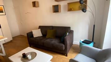Een woonkamer met een bruine bank, een grijze fauteuil, een witte salontafel en een vloerlamp.