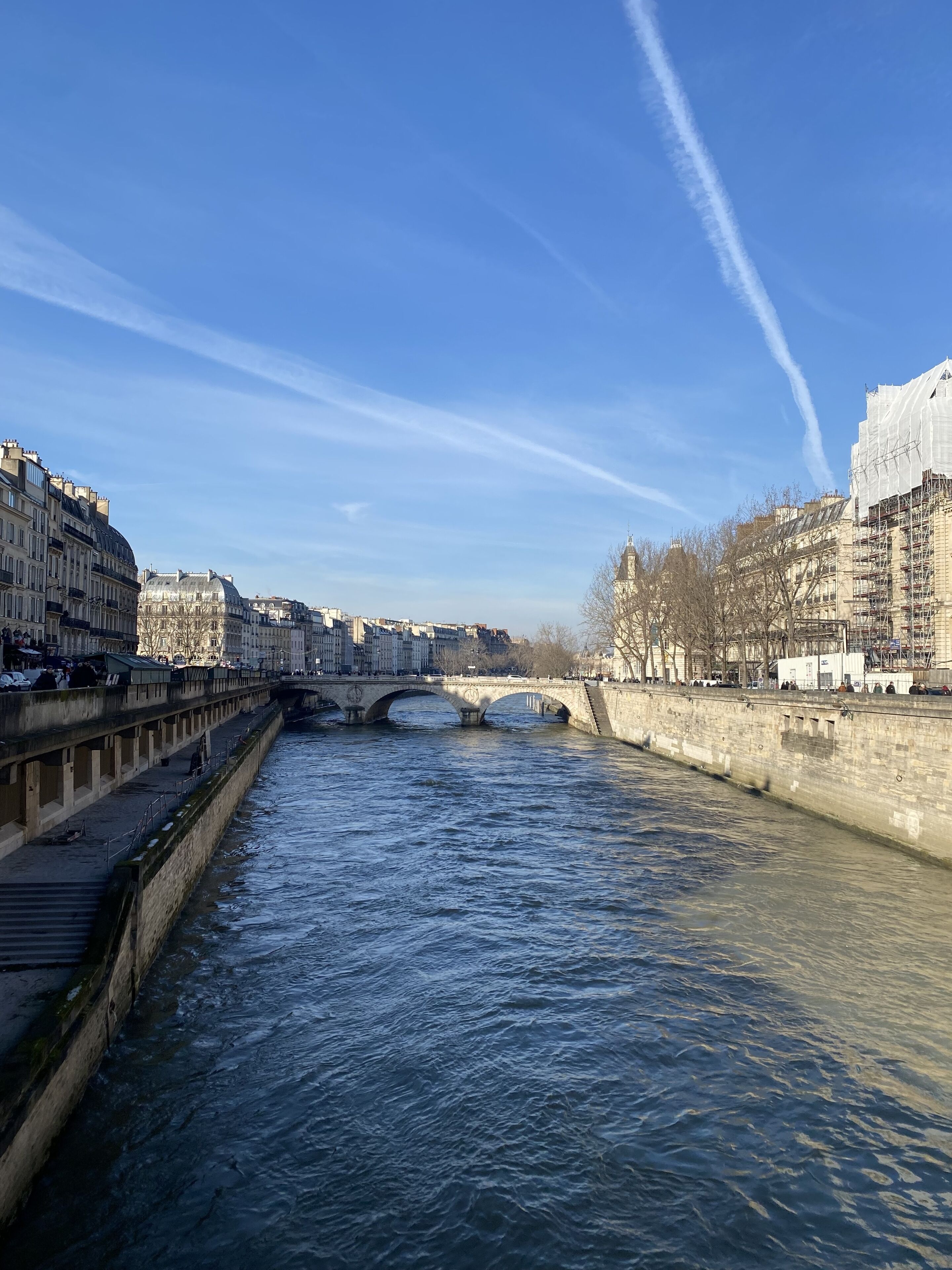 Une rivière traversée par un pont de pierre, des bâtiments de part et d’autre, et un ciel dégagé.