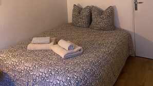 A bedroom with a patterned bedspread, two pillows, a wall-mounted lamp, and a door. - Pretty cocoon canal St Martin (Paris)