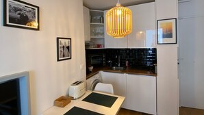 A compact kitchen with white cabinets, a wooden ceiling, a dining table with chairs, and a hanging pendant light. - Pretty cocoon canal St Martin (Paris)