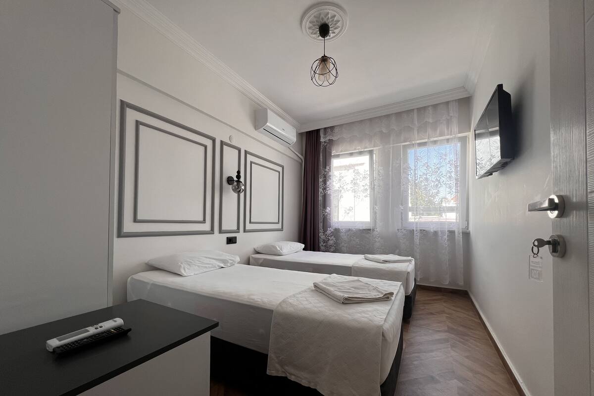 A hotel room with two beds, a desk, a TV, and a ceiling fan.