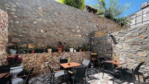 Un patio al aire libre con paredes de piedra, suelo de baldosas y varias mesas y sillas.