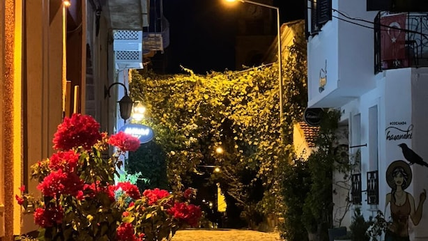 Una calle estrecha de noche con un cartel que dice 'HÜYA' y un mural en el edificio.