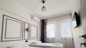 Habitación de hotel con dos camas, una lámpara en el techo, equipo de aire acondicionado, ventana con cortinas y televisor montado en la pared.