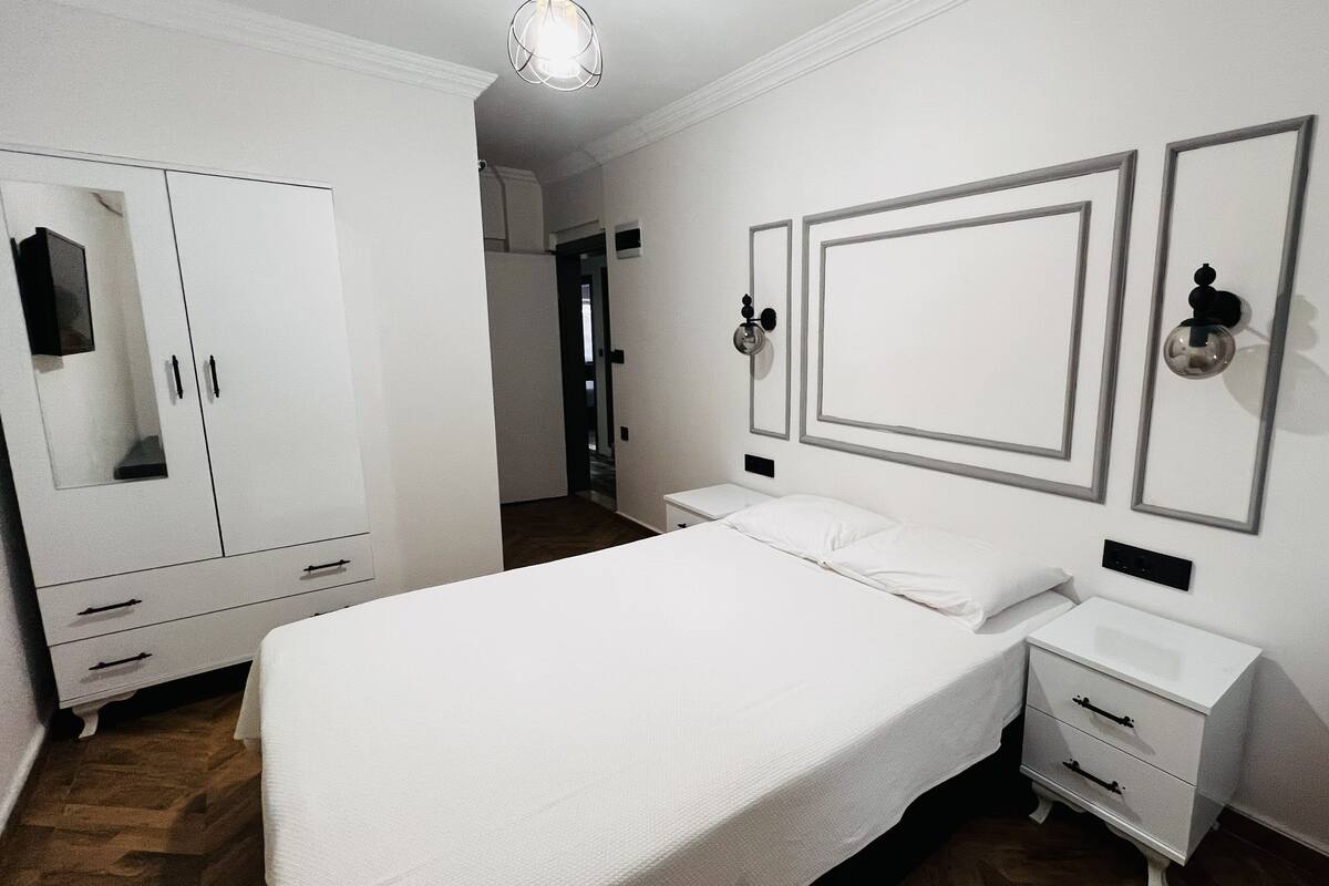 A hotel room with a large bed, a wardrobe, a bedside table, and a mirror.