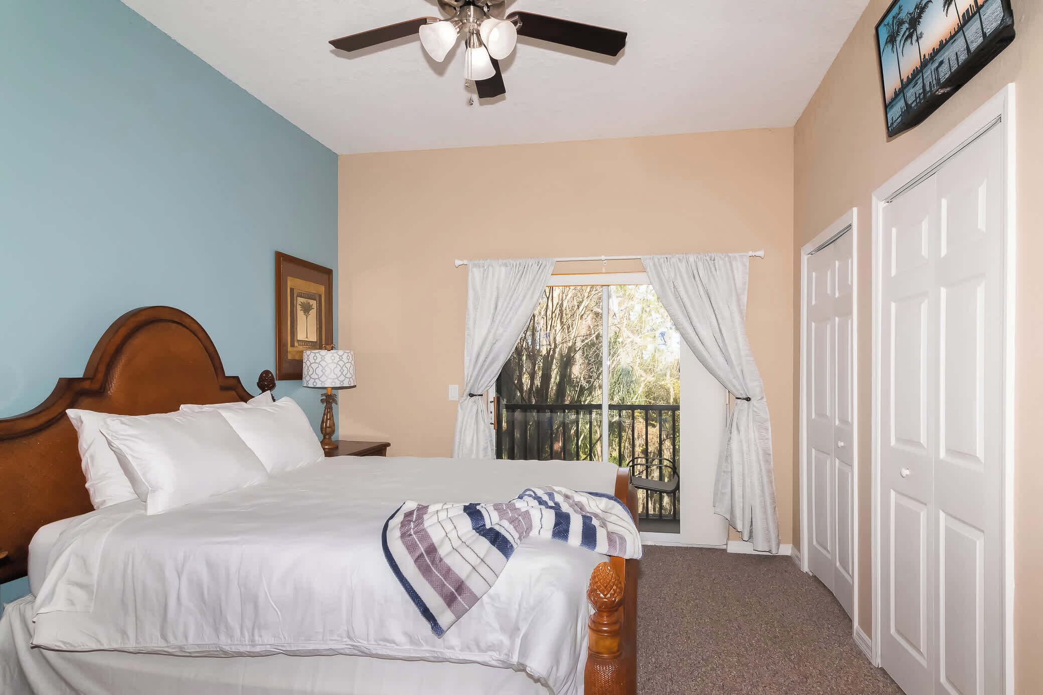 A bedroom with a bed, a ceiling fan, a window with curtains, and a door.