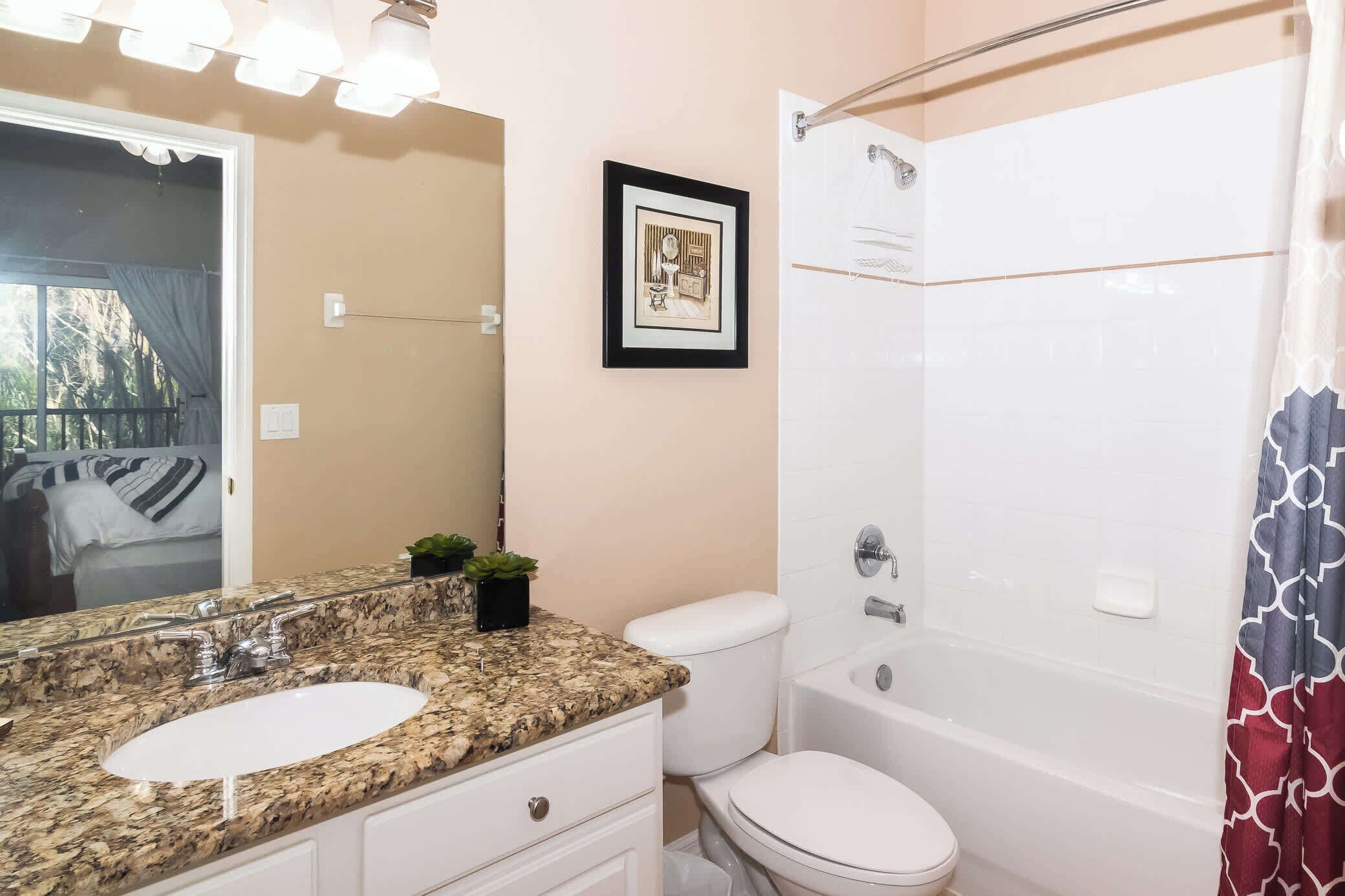 A bathroom with a granite countertop sink, white toilet, and a bathtub with a shower curtain.