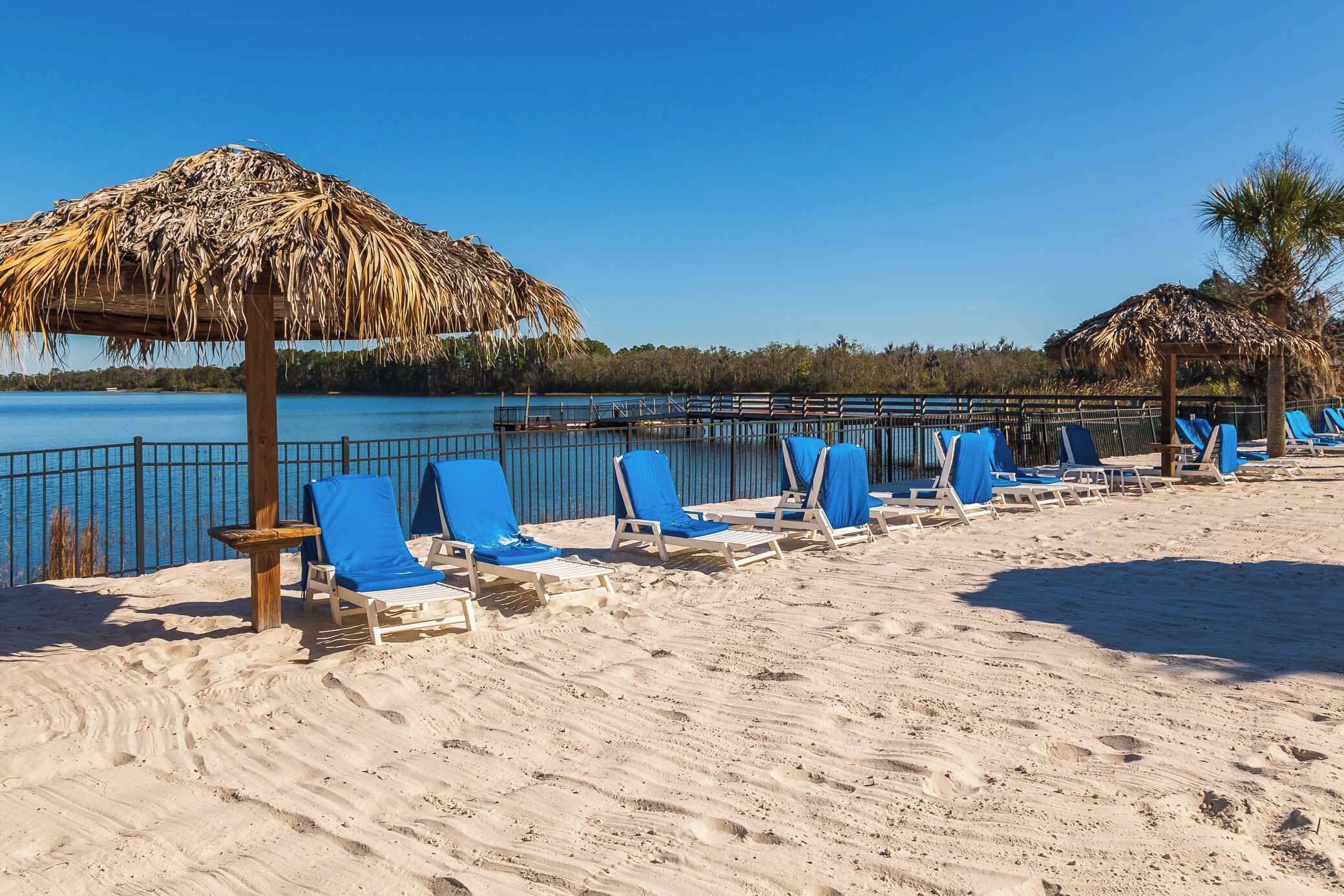A beach with sun loungers and thatched umbrellas, a wooden fence, and a clear view of the water.