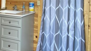 A wooden cabin bathroom with a white vanity, a shower curtain, and a ceiling-mounted light fixture. - The Cow Lodge (Clark)