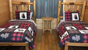 A cabin-style bedroom with two wooden beds, a small wooden table, and a window with curtains. - The Cow Lodge (Clark)