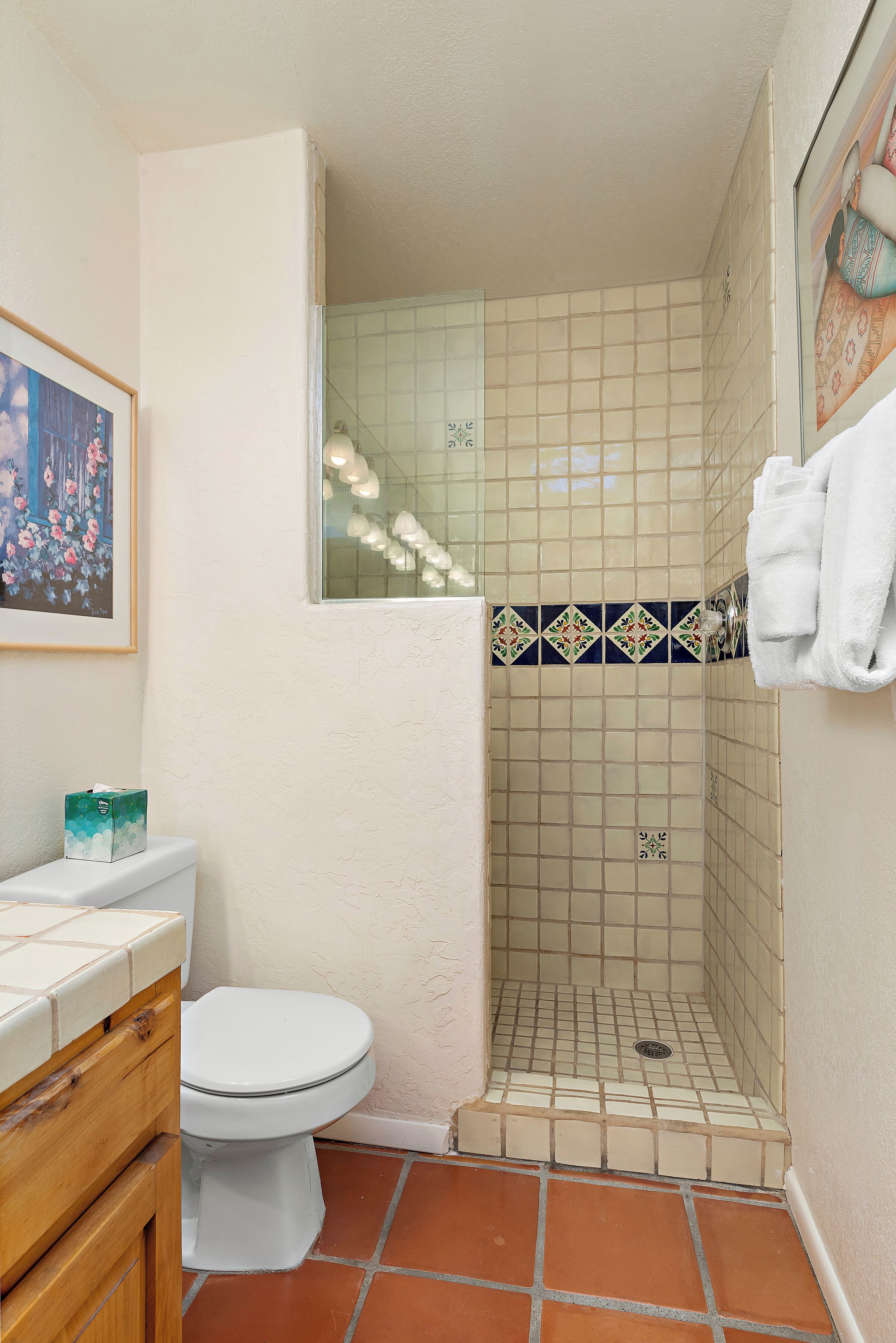 A bathroom with a toilet, a shower with tiled walls, a wooden vanity, and a framed picture on the wall.
