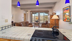 A kitchen with a stove, a dining area with chairs, and a view of the outside through large windows. - Fort Marcy 10 | Walk to Plaza | Kiva Fireplace | Full Kitchen | Hot Tub | Pool | Single Level (Santa Fe)
