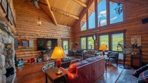 L’intérieur d’une cabane en rondins, avec un mur en pierre, un plancher en bois, un canapé en cuir rouge, un téléviseur et un ventilateur.