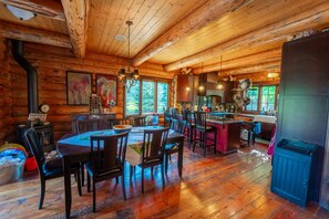 A rustic cabin interior with a wooden dining area, kitchen, and large windows. - Shangrilog - Cabin with Mountain View & Lake Front Property (Troy)