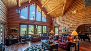 L’intérieur d’une cabane en rondins présente un grand espace de vie, des planchers en bois et de grandes fenêtres qui offrent une vue sur l’extérieur.