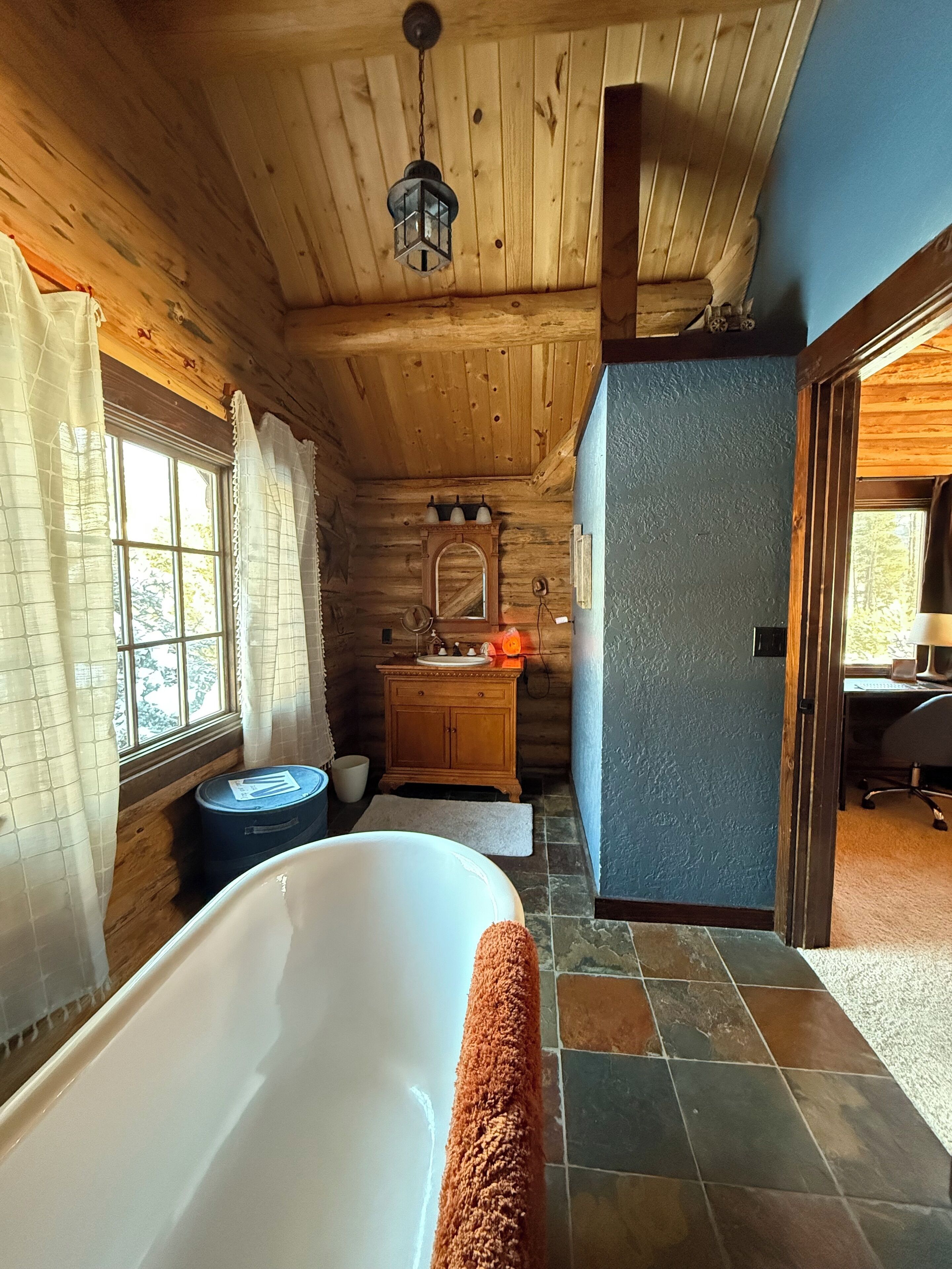 Un baño de cabaña de madera con bañera, tocador y espejo.