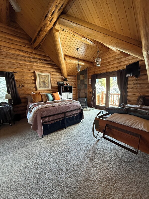Une chambre dans un chalet en rondins, avec un lit, un banc, une cheminée et un mur en pierre.