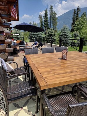 An outdoor patio with a wooden table and wicker chairs, surrounded by a wooden deck and a view of mountains. - Shangrilog - Cabin with Mountain View & Lake Front Property (Troy)