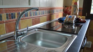Una cocina con un lavamanos de acero inoxidable, salpicadero de azulejos y encimera con productos envasados.