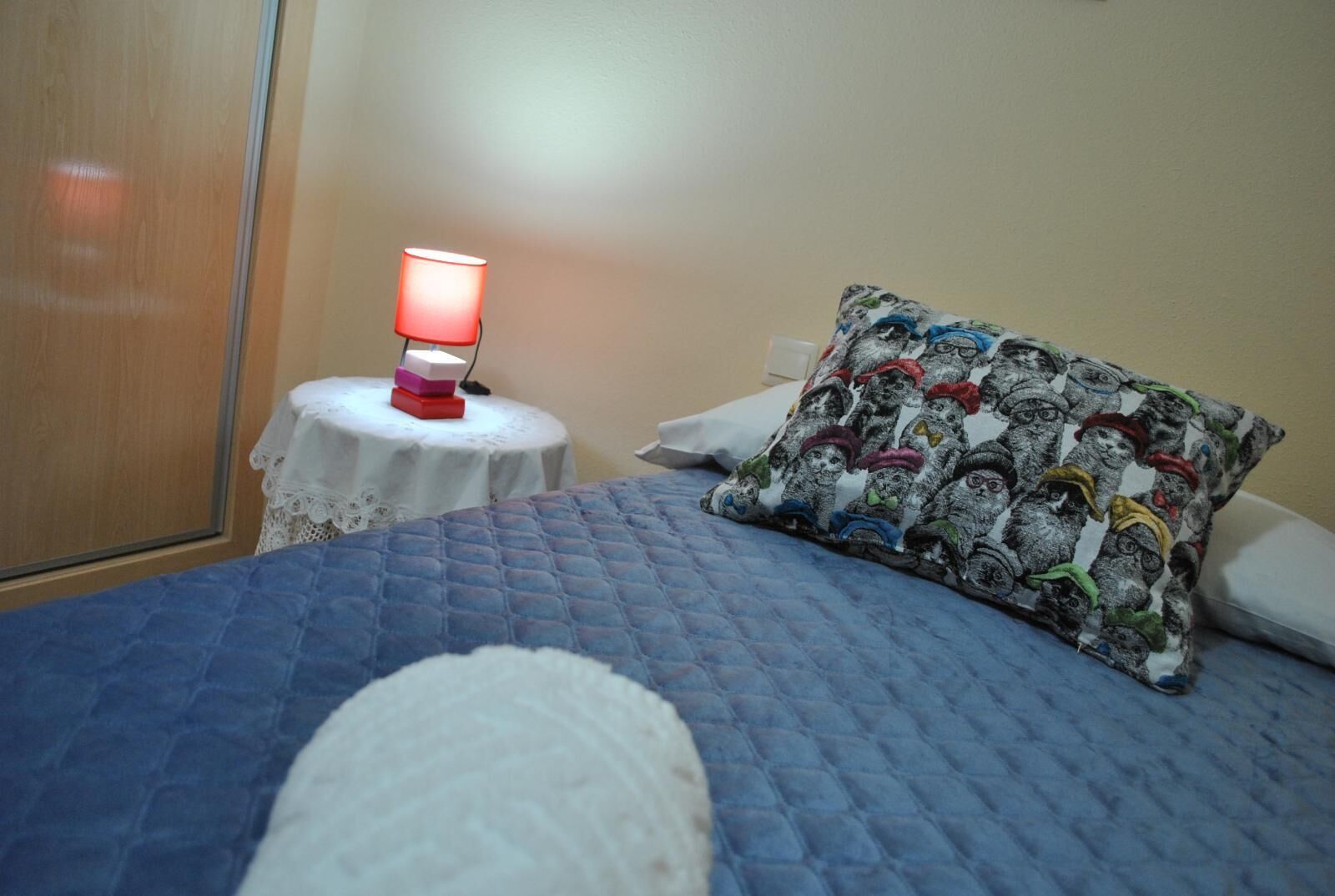 Una cama con un edredón azul, una almohada blanca y una almohada con diseños de gatos.