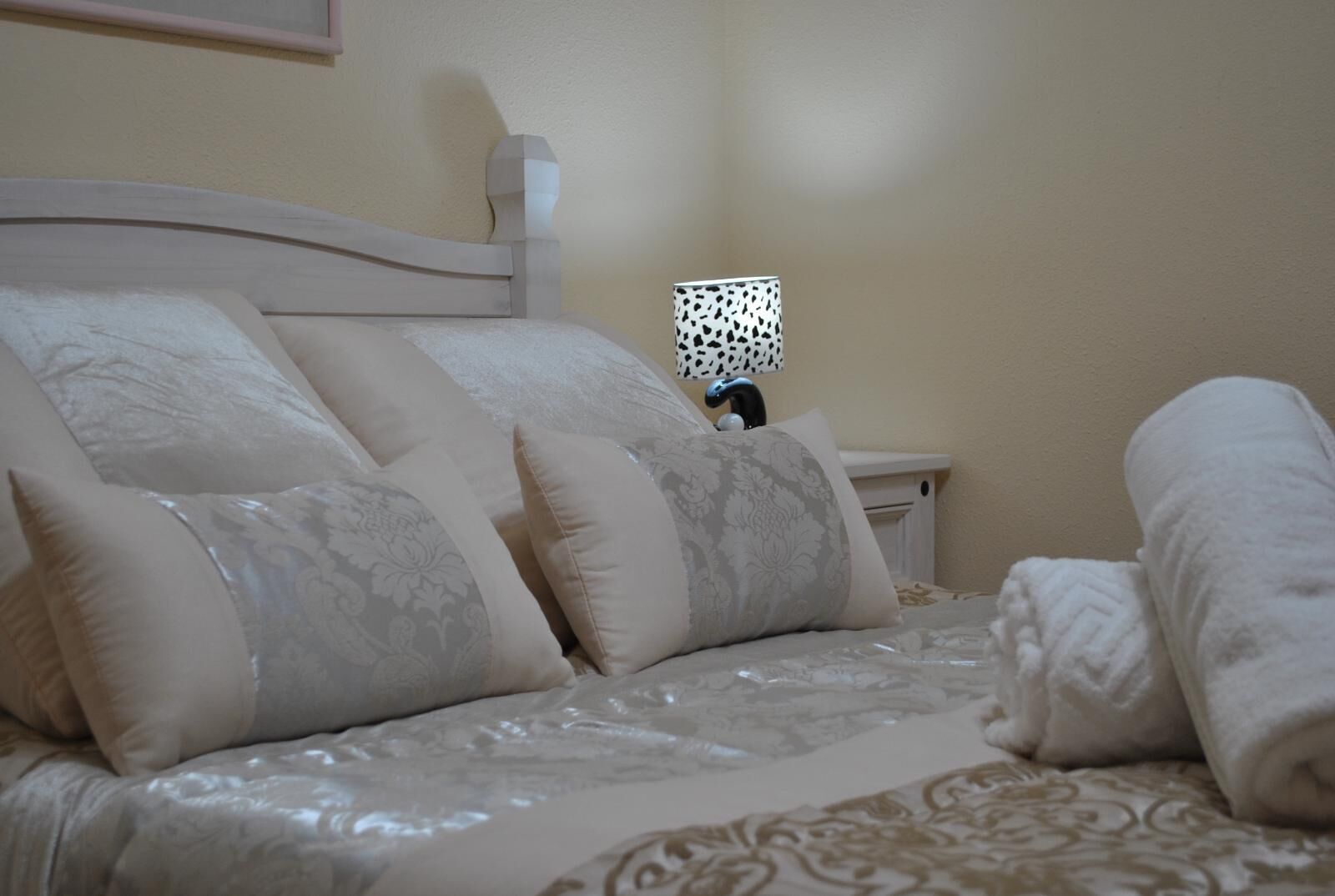 A neatly made bed with a patterned bedspread, a headboard, and a nightstand with a lamp.