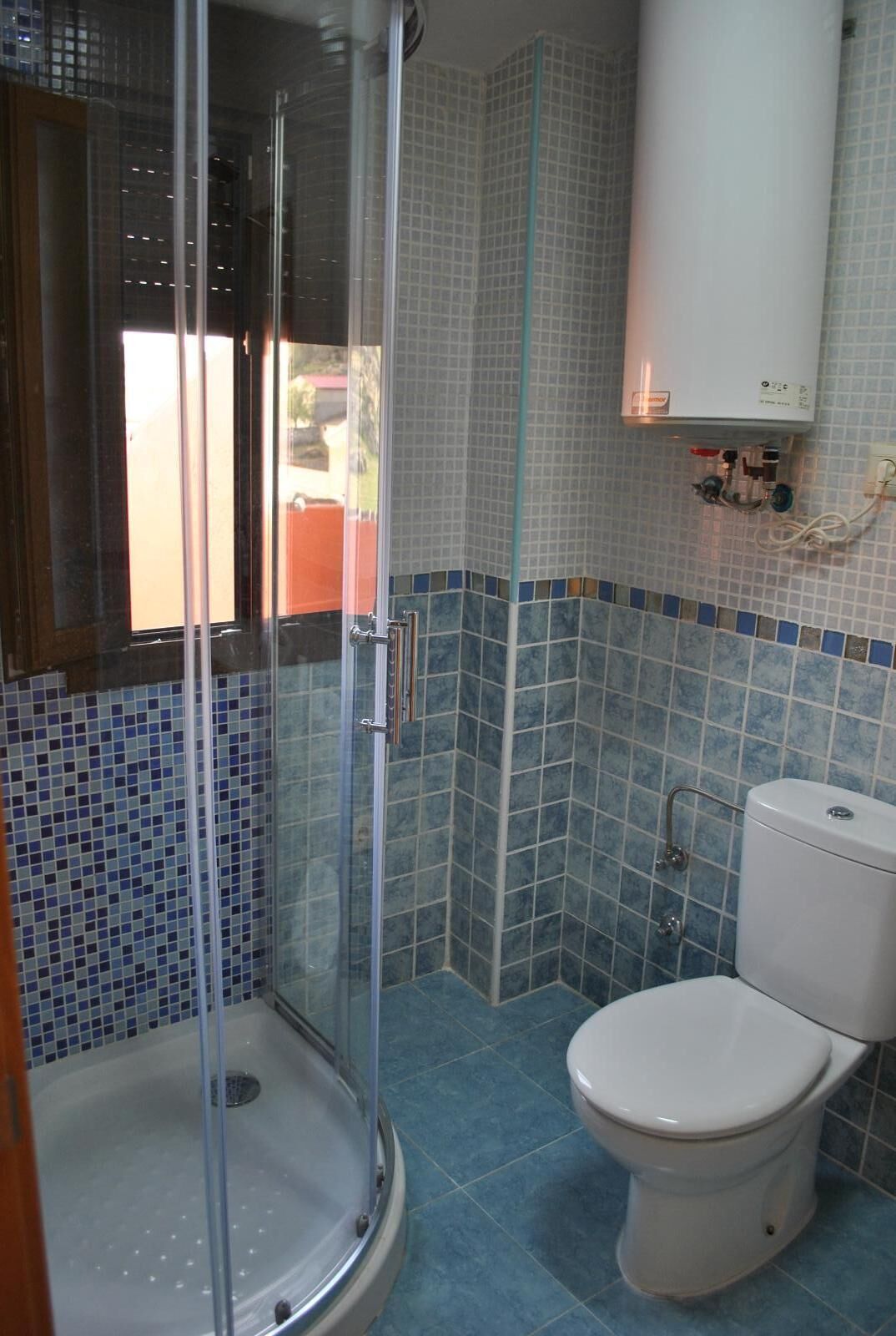 Un baño con ducha envuelta en vidrio, inodoro y paredes de azulejos.