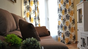 Una sala de estar con un sofá marrón, dos cojines marrones, una planta pequeña verde y un mueble con puertas de vidrio.