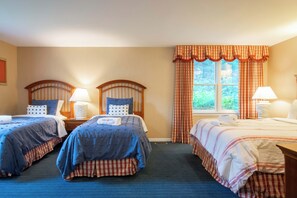 Habitación de hotel con dos camas, cada una con cabecera, lámparas de noche y ventana con cortinas.