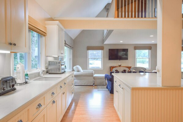 A spacious kitchen with modern appliances, a dining area with a high table, and a view of the outdoors. - Short Walk to Private Beach! (West Yarmouth)