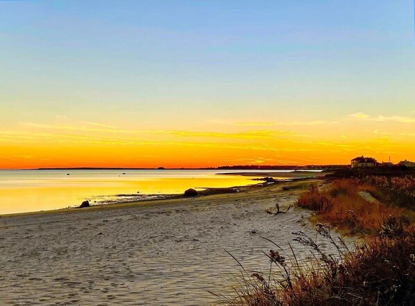A beach with a calm sea, a clear sky, and a distant shoreline.