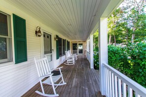 A covered porch with white rocking chairs and a wooden floor.