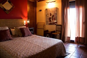 Una cama bien hecha con una colcha estampada con motivos florales, un cabecero de madera y una lámpara fijada a la pared.