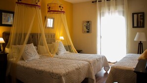 Habitación de hotel con dos camas, cada una con dosel. Hay una pequeña mesa y una silla en la esquina.