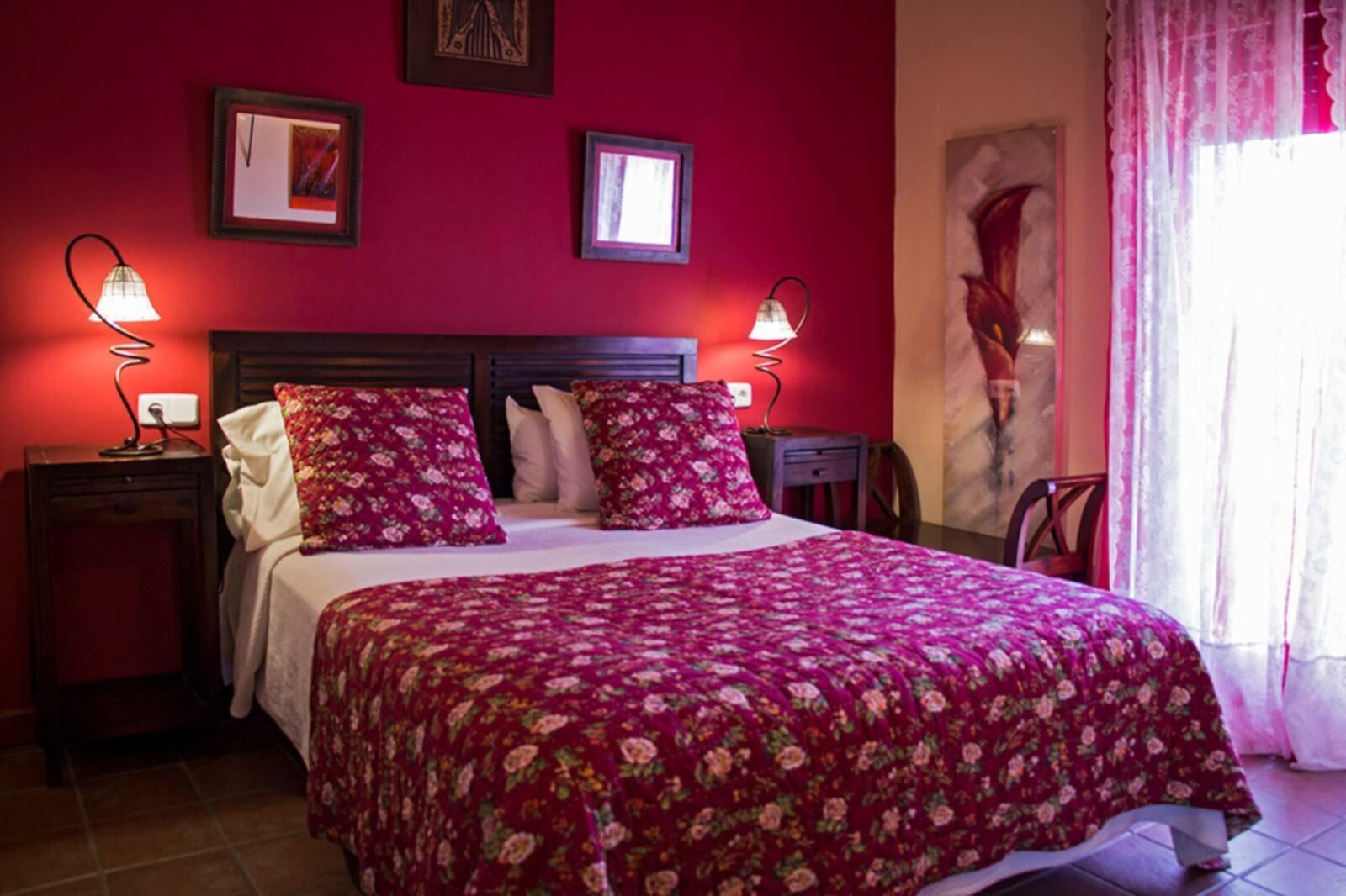Una camera da letto con copriletto floreale, due comodini con lampade, una testiera in legno e opere d'arte alle pareti.