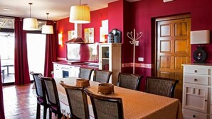 Un comedor con una mesa dispuesta para seis personas, rodeada de sillas. Se observa una cocina con estufa y armarios al fondo.