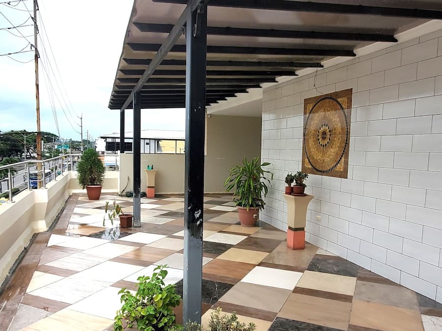A covered outdoor area with tiled flooring, potted plants, and a wall-mounted artwork.