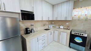 Una cocina con refrigerador, estufa, microondas, licuadora y pileta.