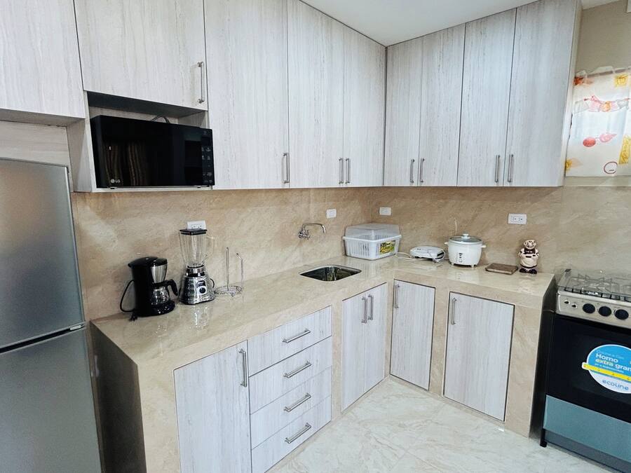 A kitchen with a refrigerator, stove, microwave, blender, and sink.