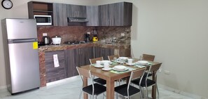 A compact kitchen with a refrigerator, microwave, stove, and sink. There is a dining table set with plates, cups, and a blender. - NCG Comegua 1 (Guayaquil)