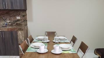 Un comedor con una mesa de madera dispuesta para cuatro personas, rodeada de sillas metálicas, en una habitación con suelo de mármol y armarios de madera oscura.
