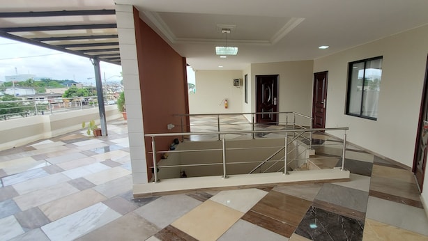 Pasillo de hotel con piso de baldosas, una escalera con barandillas de metal y puertas que dan a las habitaciones.