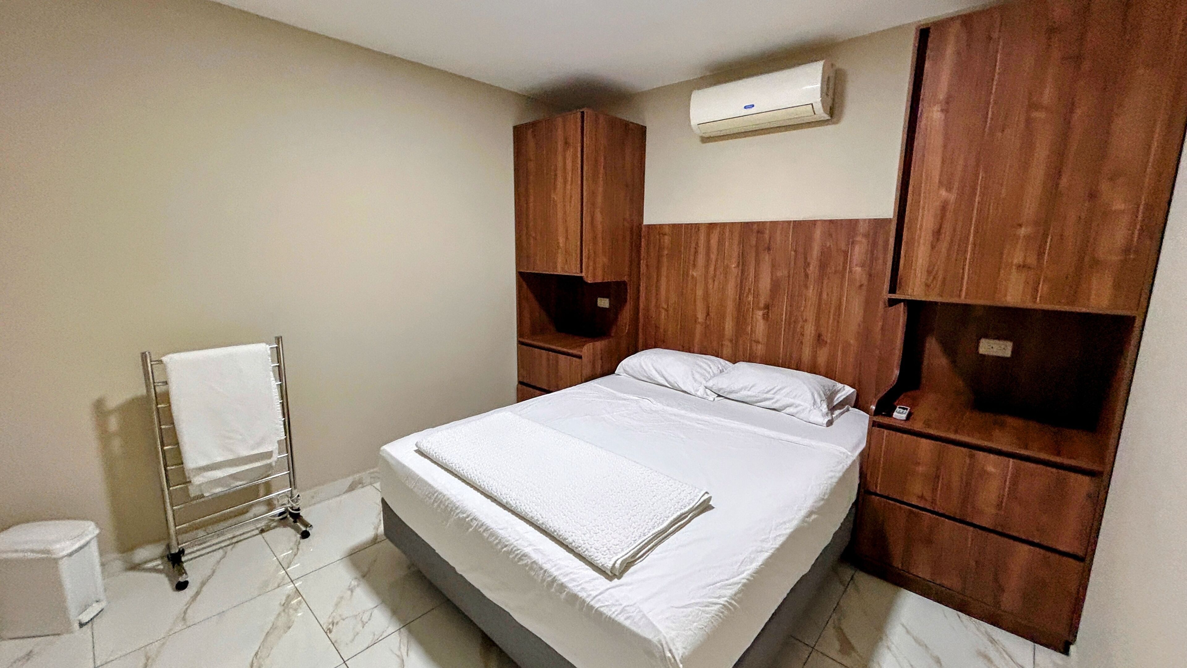 A bedroom with a bed, a towel rack, a toilet, and wooden cabinets.