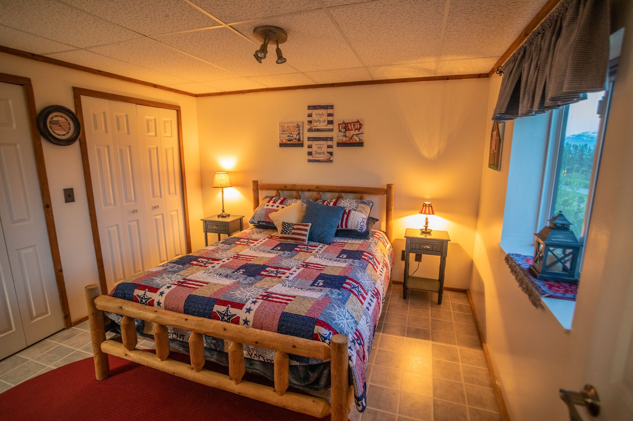 A bedroom with a wooden bed, two bedside lamps, a quilt, and a window with a view.