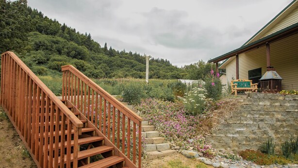 A wooden staircase leading to a stone wall with a bench and a lantern. - Otter Stop Inn! Ocean and mountain views from every window! (Homer)