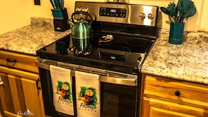 A kitchen with a stainless steel stove, a kettle, and a coffee maker. There are wooden cabinets and a granite countertop. - Otter Stop Inn! Ocean and mountain views from every window! (Homer)