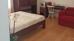 Ein Schlafzimmer mit einem Bett, einem Schreibtisch mit Fernseher, einem roten Sofa und einem Holzschrank.