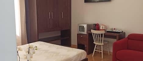 Un dormitorio con cama, escritorio con televisor, sofá rojo y armario de madera.