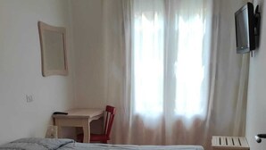 Ein Schlafzimmer mit Bett, Schreibtisch, Stuhl, Fernseher und einem Fenster mit Vorhängen.